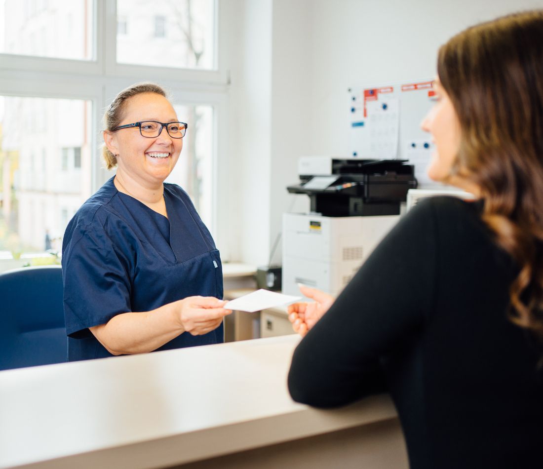 Eine Empfangsmitarbeiterin im Gespräch mit einer Patientin.
